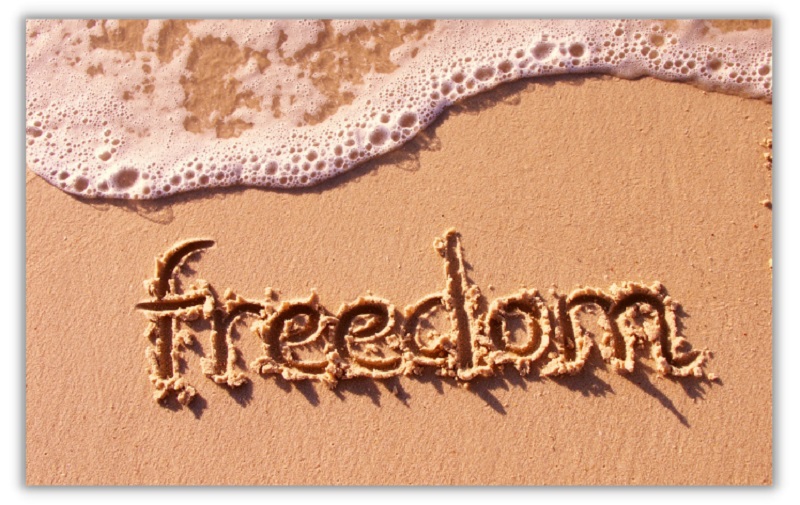 freedom drawn in sand on beach with wave coming in